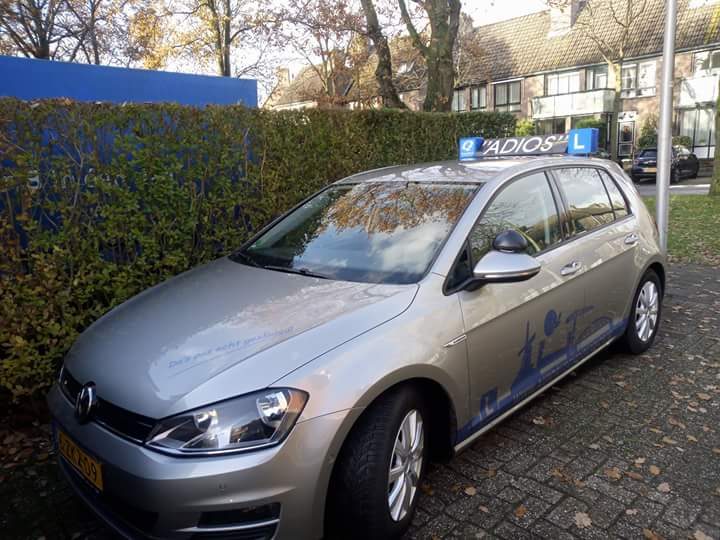 Lesauto van Autorijschool Adios, een Volkswagen Golf met Adios-belettering en blauwe L-daklichtbak